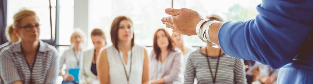 Woman speaker talking to a group of business-dressed people with lanyards on