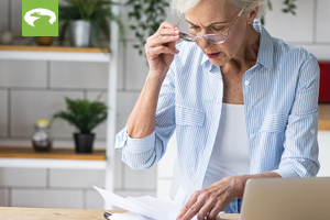 elderly woman paying bills on a laptop and looking at papers
